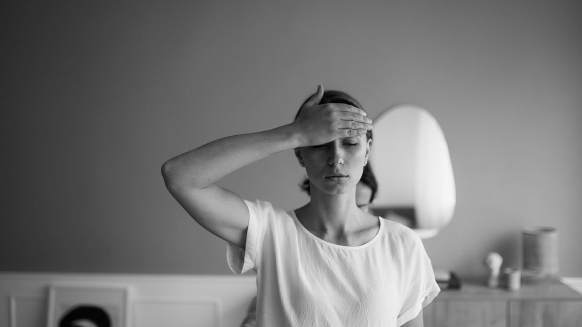 Black and white image of a woman with her hand on forehead, eyes closed and serene.